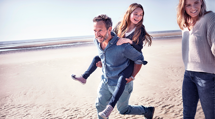 Deux femmes et un homme souriants marchant sur la plage.