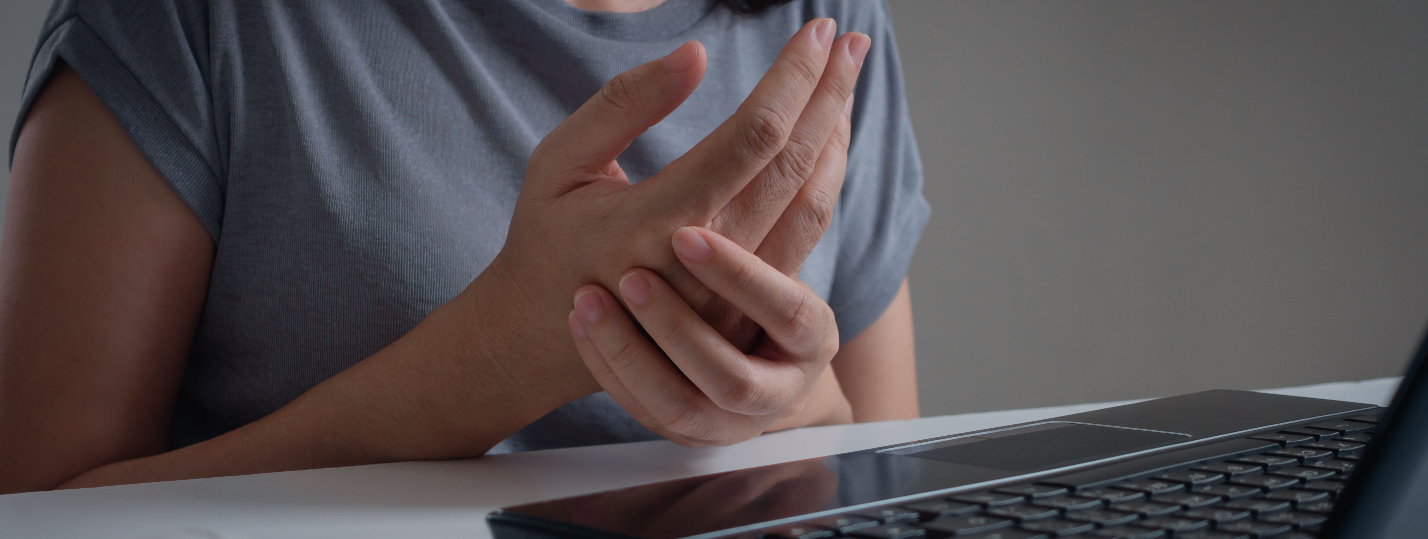 Personne devant un ordinateur portable, tenant son poignet avec l'autre main, montrant une gêne ou une douleur.
