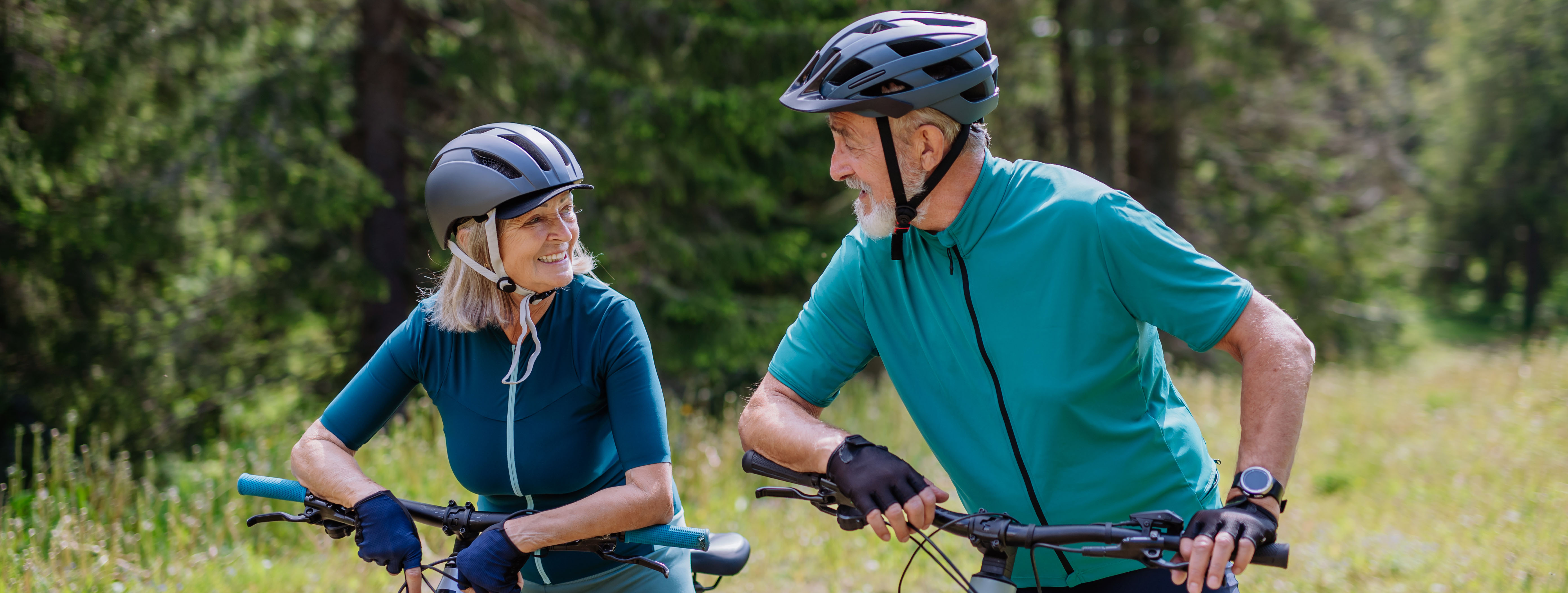 Couple âgé portant des casques de vélo, souriant et discutant en faisant du vélo dans la nature.